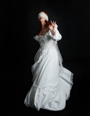 close up portrait beautiful female model wearing antique white historical ghost bride wedding dress gown, a veiled mask blindfold covering face. isolated figure on dark studio background, hand gesture