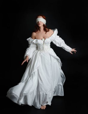 close up portrait beautiful female model wearing antique white historical ghost bride wedding dress gown, a veiled mask blindfold covering face. isolated figure on dark studio background, hand gesture