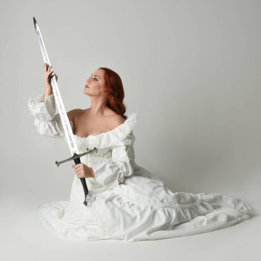 Tam boy portre, tarihi beyaz fantezi gelinlik giyen güzel kadın manken, kılıç tutan peri masalı balosu elbisesi. Stüdyonun arka planında izole bir poz.
