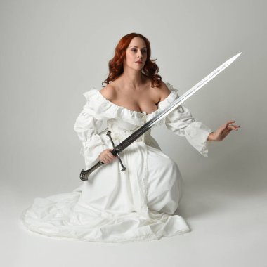 Tam boy portre, tarihi beyaz fantezi gelinlik giyen güzel kadın manken, kılıç tutan peri masalı balosu elbisesi. Stüdyonun arka planında izole bir poz.
