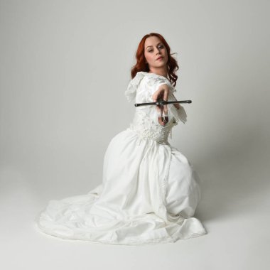 Tam boy portre, tarihi beyaz fantezi gelinlik giyen güzel kadın manken, kılıç tutan peri masalı balosu elbisesi. Stüdyonun arka planında izole bir poz.