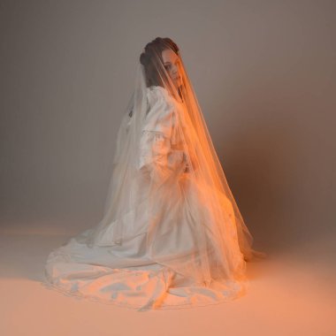 Tam boy portre, tarihi beyaz fantezi gelinlik giyen güzel kadın model, kumaş peçeli peri masalı balo elbisesi. Altın parıldayan stüdyo arka planında izole bir poz.