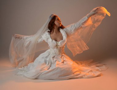 Tam boy portre, tarihi beyaz fantezi gelinlik giyen güzel kadın model, kumaş peçeli peri masalı balo elbisesi. Altın parıldayan stüdyo arka planında izole bir poz.