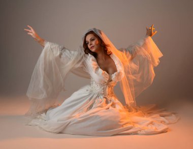 Tam boy portre, tarihi beyaz fantezi gelinlik giyen güzel kadın model, kumaş peçeli peri masalı balo elbisesi. Altın parıldayan stüdyo arka planında izole bir poz.