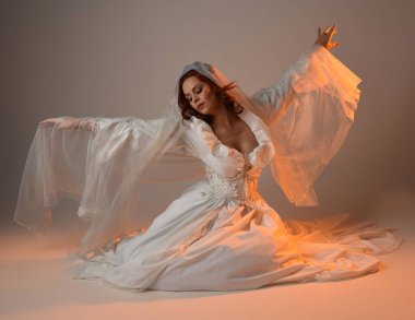 Tam boy portre, tarihi beyaz fantezi gelinlik giyen güzel kadın model, kumaş peçeli peri masalı balo elbisesi. Altın parıldayan stüdyo arka planında izole bir poz.