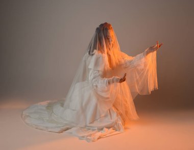 Tam boy portre, tarihi beyaz fantezi gelinlik giyen güzel kadın model, kumaş peçeli peri masalı balo elbisesi. Altın parıldayan stüdyo arka planında izole bir poz.