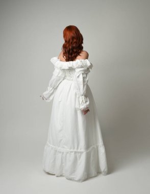 Tam boy, kızıl saçlı, tarihi fantezi gelinlik giyen bir model. Peri masalı balosu elbisesi. Kameradan uzaklaşan poz, beyaz stüdyo arka planında izole bir figür