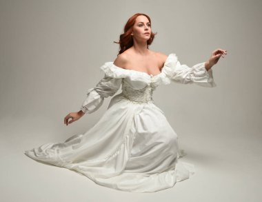 Tarihi beyaz fantezi gelinlik, peri masalı balosu elbisesi giymiş güzel bir kadın model. İzole bir poz. El hareketleriyle beyaz stüdyo arka planına duygusal olarak uzanıyor..