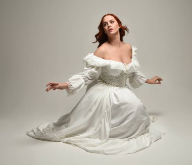 Tarihi beyaz fantezi gelinlik, peri masalı balosu elbisesi giymiş güzel bir kadın model. İzole bir poz. El hareketleriyle beyaz stüdyo arka planına duygusal olarak uzanıyor..