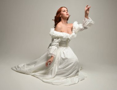Tarihi beyaz fantezi gelinlik, peri masalı balosu elbisesi giymiş güzel bir kadın model. İzole bir poz. El hareketleriyle beyaz stüdyo arka planına duygusal olarak uzanıyor..