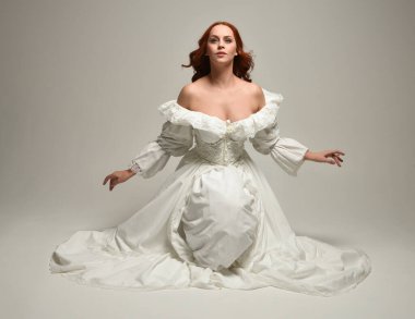 Tarihi beyaz fantezi gelinlik, peri masalı balosu elbisesi giymiş güzel bir kadın model. İzole bir poz. El hareketleriyle beyaz stüdyo arka planına duygusal olarak uzanıyor..