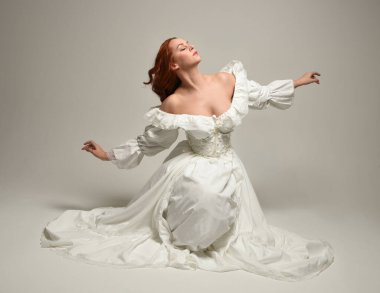 Tarihi beyaz fantezi gelinlik, peri masalı balosu elbisesi giymiş güzel bir kadın model. İzole bir poz. El hareketleriyle beyaz stüdyo arka planına duygusal olarak uzanıyor..