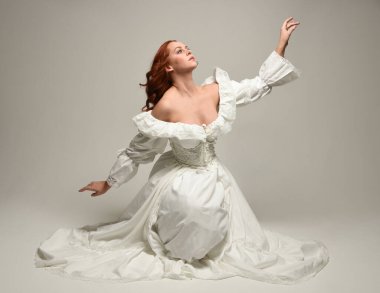 Tarihi beyaz fantezi gelinlik, peri masalı balosu elbisesi giymiş güzel bir kadın model. İzole bir poz. El hareketleriyle beyaz stüdyo arka planına duygusal olarak uzanıyor..