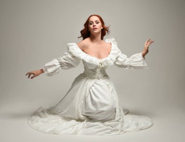 Tarihi beyaz fantezi gelinlik, peri masalı balosu elbisesi giymiş güzel bir kadın model. İzole bir poz. El hareketleriyle beyaz stüdyo arka planına duygusal olarak uzanıyor..