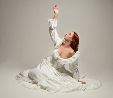 Tarihi beyaz fantezi gelinlik, peri masalı balosu elbisesi giymiş güzel bir kadın model. İzole bir poz. El hareketleriyle beyaz stüdyo arka planına duygusal olarak uzanıyor..