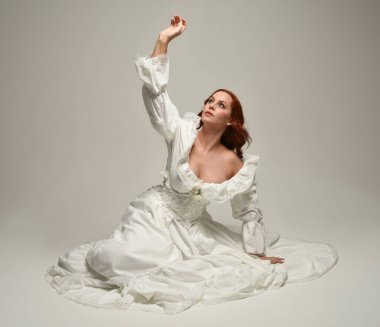 Tarihi beyaz fantezi gelinlik, peri masalı balosu elbisesi giymiş güzel bir kadın model. İzole bir poz. El hareketleriyle beyaz stüdyo arka planına duygusal olarak uzanıyor..