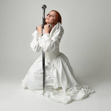 Tam boy portre, tarihi beyaz fantezi gelinlik giyen güzel kadın manken, kılıç tutan peri masalı balosu elbisesi. Stüdyonun arka planında izole bir poz.