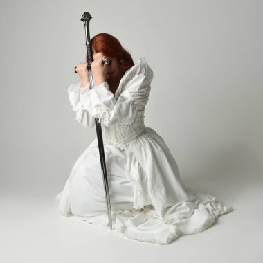 Tam boy portre, tarihi beyaz fantezi gelinlik giyen güzel kadın manken, kılıç tutan peri masalı balosu elbisesi. Stüdyonun arka planında izole bir poz.