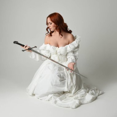 Tam boy portre, tarihi beyaz fantezi gelinlik giyen güzel kadın manken, kılıç tutan peri masalı balosu elbisesi. Stüdyonun arka planında izole bir poz.