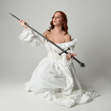 Tam boy portre, tarihi beyaz fantezi gelinlik giyen güzel kadın manken, kılıç tutan peri masalı balosu elbisesi. Stüdyonun arka planında izole bir poz.