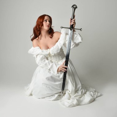 Tam boy portre, tarihi beyaz fantezi gelinlik giyen güzel kadın manken, kılıç tutan peri masalı balosu elbisesi. Stüdyonun arka planında izole bir poz.