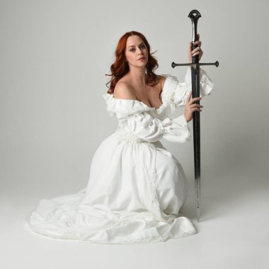 Tam boy portre, tarihi beyaz fantezi gelinlik giyen güzel kadın manken, kılıç tutan peri masalı balosu elbisesi. Stüdyonun arka planında izole bir poz.