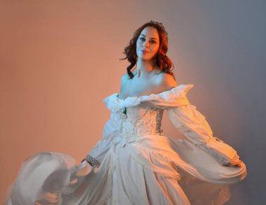 Tarihi fantezi gelinlik, peri masalı balosu elbisesi ve altın kraliyet tacı giyen güzel kızıl saçlı manken. Renkli stüdyo arka planında dans eden izole şahsiyet