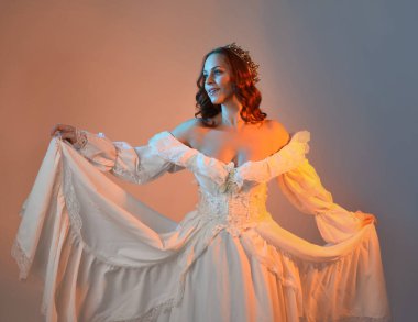 Tarihi fantezi gelinlik, peri masalı balosu elbisesi ve altın kraliyet tacı giyen güzel kızıl saçlı manken. Renkli stüdyo arka planında dans eden izole şahsiyet