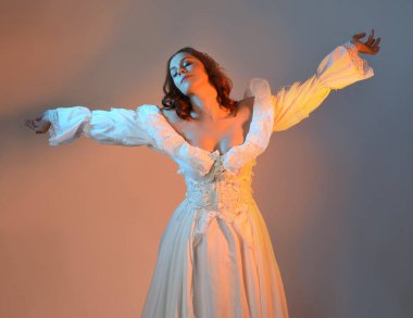 Tarihi fantezi gelinlik, peri masalı balosu elbisesi ve altın kraliyet tacı giyen güzel kızıl saçlı manken. Renkli stüdyo arka planında dans eden izole şahsiyet