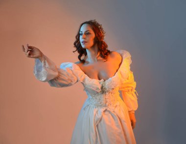 Tarihi fantezi gelinlik, peri masalı balosu elbisesi ve altın kraliyet tacı giyen güzel kızıl saçlı manken. Renkli stüdyo arka planında dans eden izole şahsiyet