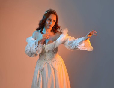 Tarihi fantezi gelinlik, peri masalı balosu elbisesi ve altın kraliyet tacı giyen güzel kızıl saçlı manken. Renkli stüdyo arka planında dans eden izole şahsiyet