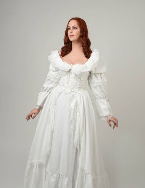 Yakın plan güzel kızıl saçlı manken tarihi fantezi gelinlik giyiyor, peri masalı balosu elbisesi giyiyor. Beyaz stüdyo arka planında izole bir figür