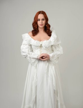 Yakın plan güzel kızıl saçlı manken tarihi fantezi gelinlik giyiyor, peri masalı balosu elbisesi giyiyor. Beyaz stüdyo arka planında izole bir figür