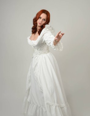 Yakın plan güzel kızıl saçlı manken tarihi fantezi gelinlik giyiyor, peri masalı balosu elbisesi giyiyor. Beyaz stüdyo arka planında izole bir figür