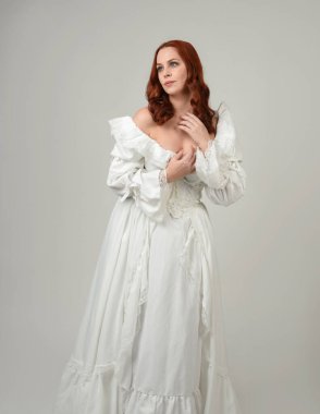 Yakın plan güzel kızıl saçlı manken tarihi fantezi gelinlik giyiyor, peri masalı balosu elbisesi giyiyor. Beyaz stüdyo arka planında izole bir figür