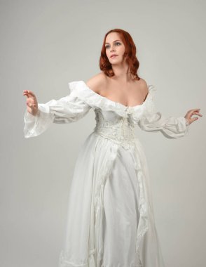 Yakın plan güzel kızıl saçlı manken tarihi fantezi gelinlik giyiyor, peri masalı balosu elbisesi giyiyor. Beyaz stüdyo arka planında izole bir figür