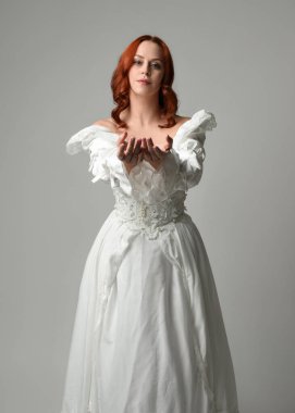 Tarihi fantezi gelinlik giyen, peri masalı balosu elbisesi giyen güzel bir kadın manken. Beyaz stüdyo arka planında yukarıdaki ışığa uzanan yalıtılmış el hareketi