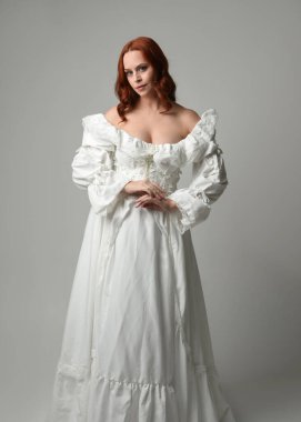 Yakın plan güzel kızıl saçlı manken tarihi fantezi gelinlik giyiyor, peri masalı balosu elbisesi giyiyor. Beyaz stüdyo arka planında izole bir figür