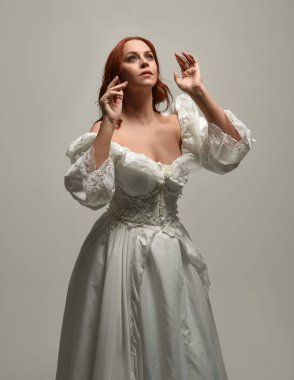 Tarihi fantezi gelinlik giyen, peri masalı balosu elbisesi giyen güzel bir kadın manken. Beyaz stüdyo arka planında yukarıdaki ışığa uzanan yalıtılmış el hareketi