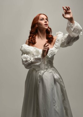 Tarihi fantezi gelinlik giyen, peri masalı balosu elbisesi giyen güzel bir kadın manken. Beyaz stüdyo arka planında yukarıdaki ışığa uzanan yalıtılmış el hareketi