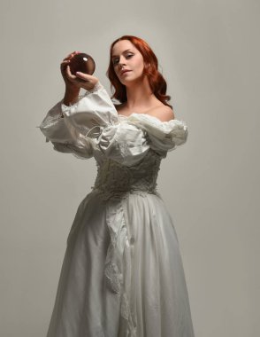 Yakın plan güzel kızıl saçlı manken tarihi beyaz fantezi gelinlik giyiyor, peri masalı elbisesi giyiyor, elinde kristal kahinler var. Beyaz arkaplanda yukarıdaki stüdyonun ışığı