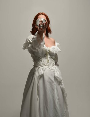 Yakın plan güzel kızıl saçlı manken tarihi beyaz fantezi gelinlik giyiyor, peri masalı elbisesi giyiyor, elinde kristal kahinler var. Beyaz arkaplanda yukarıdaki stüdyonun ışığı