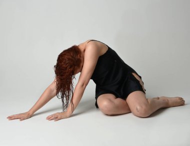 Islak, dağınık saçlı, siyah ipek cübbeli, çürük bacaklı güzel bir kadın modelin tam boy portresi. Otururken hüzünlü, hüzünlü bir pozla poz vermek. Stüdyo arkaplanındaki izole kişi.