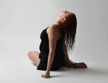 Güzel kadın modelin tam boy portresi, ıslak dağınık saçlar, sade siyah ipek bornoz, çürük bacaklar. Otururken duygusal hüzünlü bir poz verin. Stüdyo arka planında izole bir figür, koyu renkli karşıtlık gölgeleri.