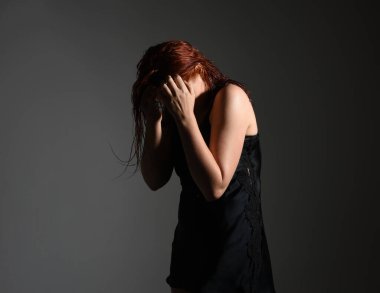 Kız modelin yakın portresi, ıslak dağınık saçlar, basit siyah ipek sabahlık, ayakta duran yan profil, gergin duygusal duruş, el hareketi. Karanlık stüdyo arka planında gölgeleri olan izole bir figür..