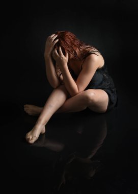 Uzun boylu, nemli saçlı, siyah, çekici bir elbise giyen bir manken. Diz çökmüş, ıslak, siyah zeminde su yansımaları olan bir poz. Karanlık stüdyo arka planında izole bir figür.