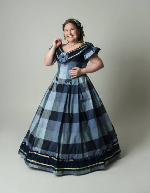 Viktorya Dönemi kadınının tarihi klasik Mavi Balo Elbisesi kostümü içinde portresi artı boyut model, tam boy ayakta duruş. Stüdyo arkaplanındaki izole kişi.