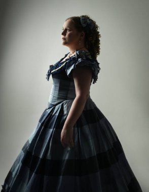 Viktorya Dönemi kadınının tarihi klasik Mavi Balo elbisesi içinde portresi artı boyut modeli, elinde gotik insan kafatası var. Stüdyo arka planında izole edilmiş koyu renk siluet figürü.