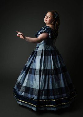 Viktorya dönemi kadınının tarihi klasik mavi balo elbisesi içinde tam boy portresi, güzel artı beden modeli. İzole edilmiş siluet figürü, uzaklaşıyor, arka plan, karanlık stüdyo arka plan..