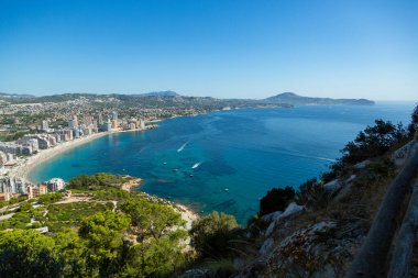 Akdeniz manzaralı dağ manzarası, mavi gökyüzü, yeşil ağaçlar ve güneşli yaz gününde İspanya 'nın Calpe plajı..